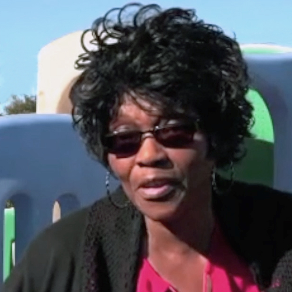 UZURV rider Shirley B. is interviewed outside. She wears sunglasses and is seated in front of playground equipment.