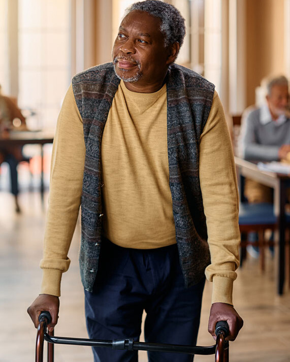 An elderly man leans on a walker for support and smiles.